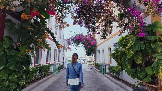 Woman walking down a picturesque alley with colorful bougainvillea flowers in Puerto de Mogan, a charming fishing village in Gran Canaria