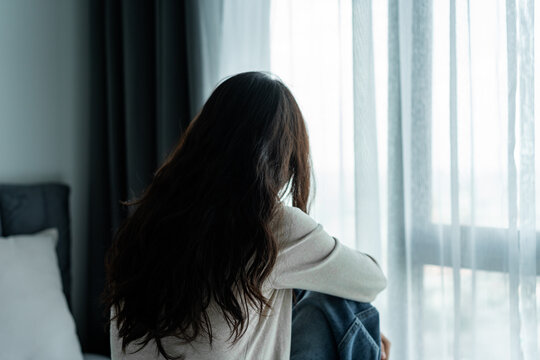 Mental health problems and depression concept: Rear view of a depressed female sitting on a bed, feeling isolated and sad at home