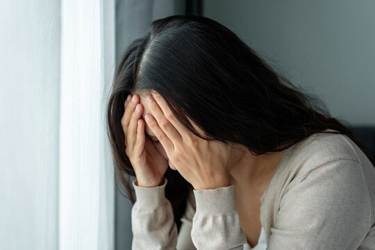 Depressed young Asian woman covering her face with hands in sadness and despair at home, Mental health problems and depression concept
