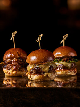 Three mini burgers are lined up on a dark, glossy bar counter, empty space