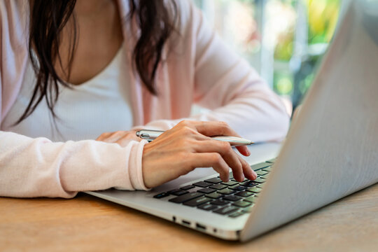 Close-up of a woman's hands taking notes and typing on a laptop, cozy work from home environment