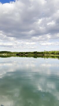 Breathtaking mirror reflection of rugged mountain peaks and fluffy cumulus clouds on a calm forest lake during golden hour
