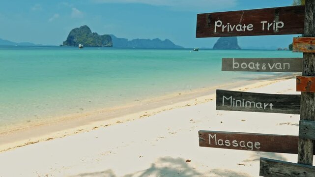 Wooden signpost indicating private trips and local services on Koh Ngai white sand beach, turquoise Andaman Sea, limestone islands background, Thailand, travel destination marketing