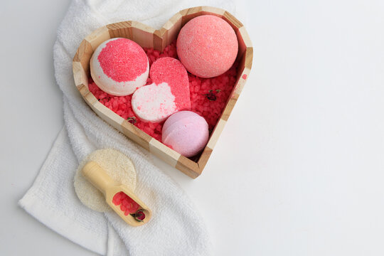 Bath bombs in heart shaped wooden box with decorative elements on soft white towel at home spa setting