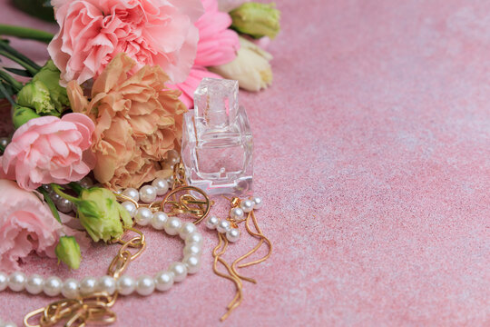 Flowers and perfume bottle arranged with jewelry on pink background in a natural light setting during daytime