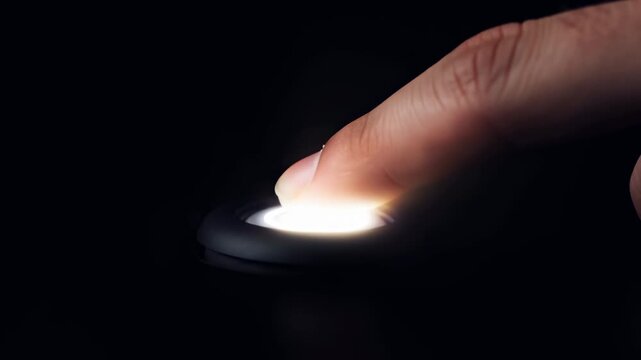 Close-up fingertip pressing glowing circular start button on dark matte surface, dramatic low-key lighting and strong contrast, showing clear contact, activation, and modern interactive control