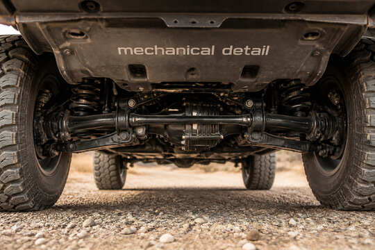 A close-up view of a vehicle's undercarriage and suspension system on a gravel surface.