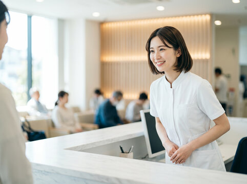 病院の受付で丁寧に笑顔を向ける制服姿の若い女性