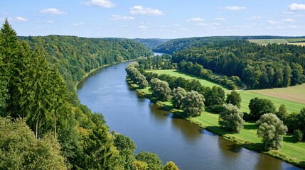 Obraz premium Scenic aerial view of a wide, winding river flowing through lush green forests and rolling hills under a clear blue sky
