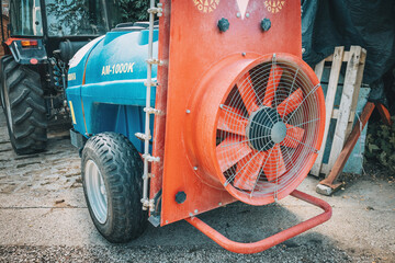 Obraz premium 7 June 2026, Sremski Karlovici, Serbia: Heavy duty tractor pulling a blue tank sprayer with a powerful red fan, ready for crop treatment and fumigation