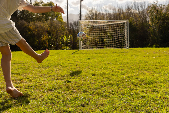 teenage boy kicking soccer ball  into net on large lawn