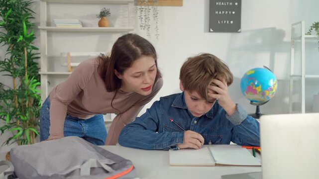 Caucasian mother helping young son with homework at living room at home.