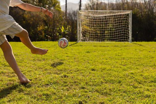 teenage boy kicking soccer ball  into net on large lawn