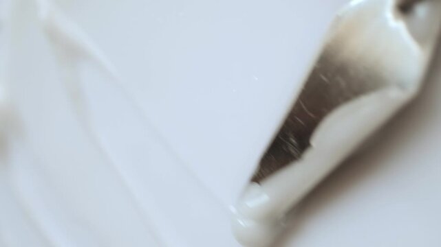 Metal spatula spreading white cosmetic cream in smooth, wavy texture macro shot