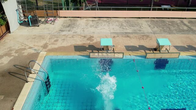 Aerial view of woman diving to outdoor swimming pool from starting block. 