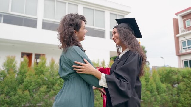 Senior Latino mother give flowers to young daughter after college graduation. 