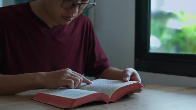 Close-up of a person reading and studying the Holy Bible at home, pointing to scripture. Concept of faith, worship, spiritual learning and connection with God. Morning devotion. 