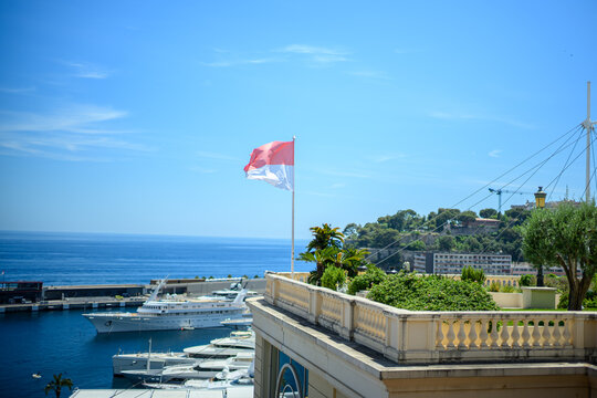 Monaco national flag waving above a luxury marina overlooking the Mediterranean Sea.