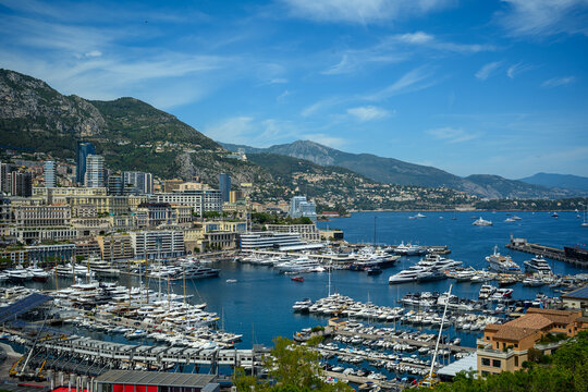 Panoramic view of Port Hercule in Monaco, showcasing luxury yachts, the Monte Carlo skyline, and the Mediterranean coastline surrounded by scenic mountains.