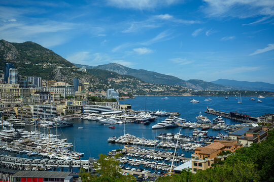 Panoramic view of Port Hercule in Monaco, showcasing luxury yachts, the Monte Carlo skyline, and the Mediterranean coastline surrounded by scenic mountains.