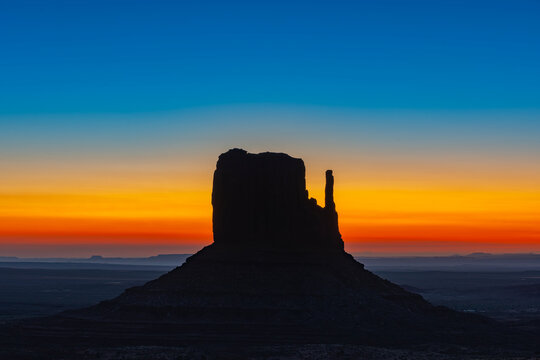 Monument Valley Butte Silhouette at Sunrise with Desert Mist and Vibrant Dawn Sky, Arizona, Utah, USA