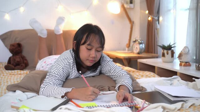 Young girl lies comfortably on bed Sketching in Notebook While Studying on Bed at Home