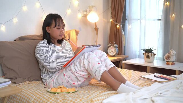 Relaxed young girl  sits comfortably on her bed, reading from a notebook while enjoying a healthy snack in a warm and cozy bedroom illuminated by soft decorative lights