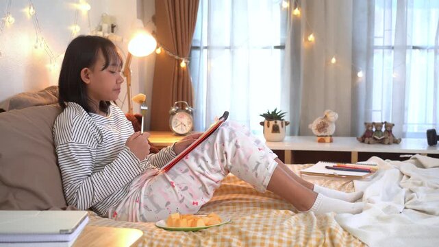 Relaxed young girl  sits comfortably on her bed, reading from a notebook while enjoying a healthy snack in a warm and cozy bedroom illuminated by soft decorative lights