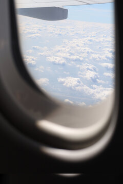 View looking through an airplane window showing the wing and fluffy white clouds