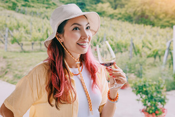 Obraz premium Happy young woman holding red wine glass at a sunny vineyard. Degustation tourism concept.