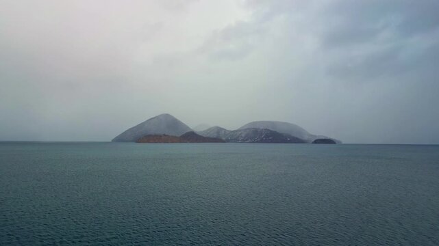 A serene aerial view of a misty volcanic island surrounded by calm dark waters under an overcast winter sky.