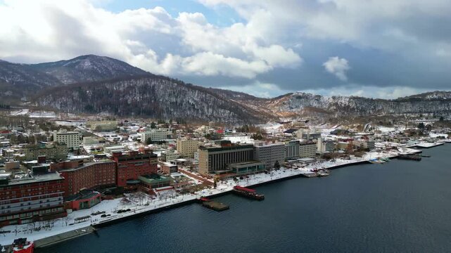 Wide angle drone footage tracking across a gorgeous snow-laden lakeside town with magnificent mountains stretching into the distance.