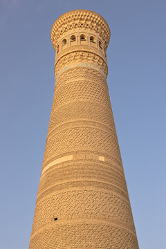 Kalyan Minaret in Bukhara with intricate brickwork patterns viewed from below against a clear blue sky. Ideal for travel publications and cultural heritage materials.
