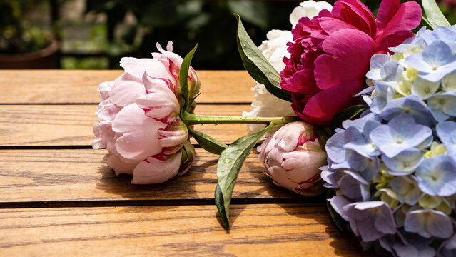Bright flowers on a wooden table with green plants in the background during daylight hours