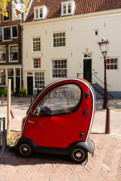 AMSTERDAM, NETHERLANDS - SEPTEMBER 05, 2025: A small red Canta LX microcar parked on a sidewalk near the city canal with historic Dutch architecture in the background