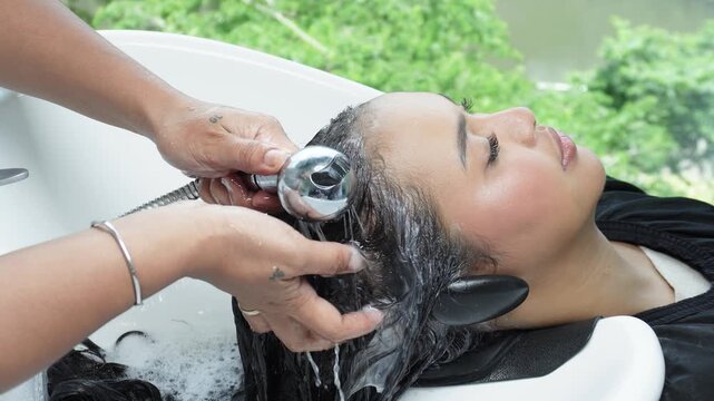 Hair stylist rinsing and shampooing hair after rebonding treatment in salon for Southeast Asian woman in her early 20s