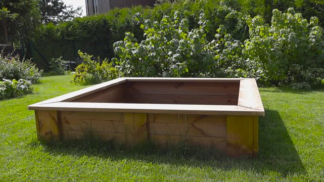 New empty wooden sandbox standing on the green grass of a backyard garden, providing an ideal play area for children's outdoor entertainment and summertime fun activities