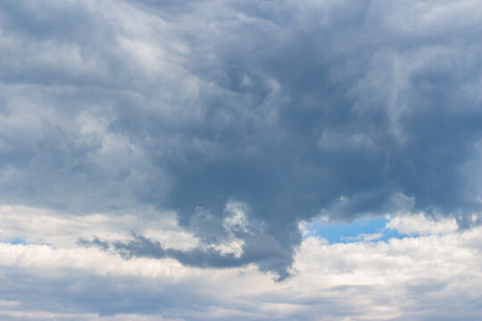 Dramatic dark storm clouds gathering in the vast sky, creating a moody atmosphere with heavy billowing formations and a small glimpse of light blue sky breaking through the gloom