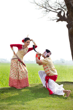 Bihu man blowing on a pepa while Bihu woman looks on 