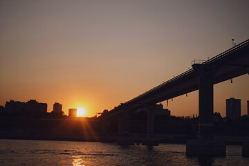Fototapeta premium Silhouette of Volgograd bridge over river at sunset. Urban landscape with road infrastructure during golden hour. City bridge cityscape view for travel and transportation background concept.