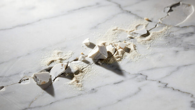 Broken white ceramic plate with cracks and chips on marble surface. Damaged porcelain dish showing fine fractures and texture details in close-up v...