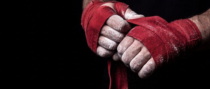 Boxer hands wrapped in thick red cotton fabric bandages covered with white chalk dust ready for intense combat sports training.
