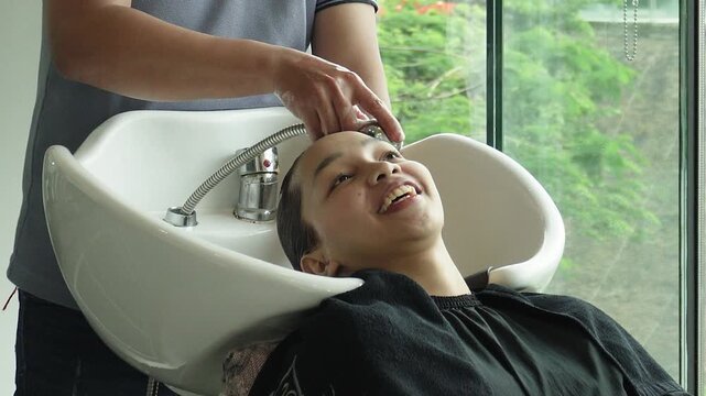 A smiling young asian woman has an animated chat with her friendly stylist while her hair is rinsed during a hair coloring treatment at a salon.