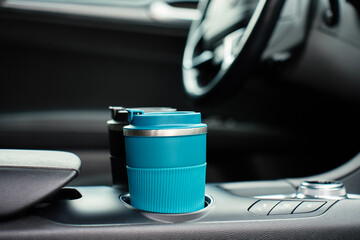 Obraz na płótnie Canvas Two reusable coffee cups in the center console cup holders inside a modern car, with the steering wheel and dashboard blurred in the background