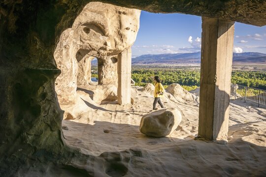 Female tourist walks around Uplistsikhe cave city exploring architectural structures. Georgia