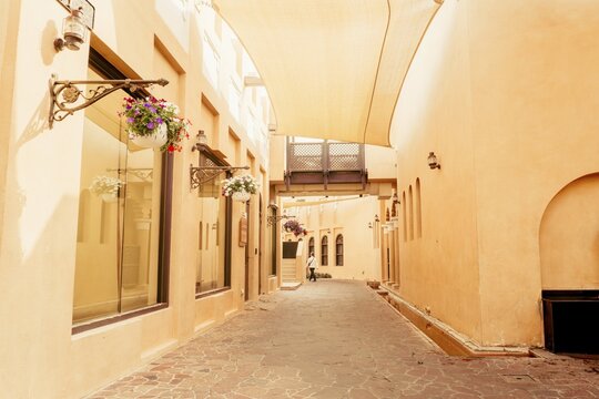 Doha, Qatar - 8th january, 2026: Narrow stone street Katara Cultural Village Doha. Traditional sand-colored buildings, hanging flower baskets, vintage wall lamps. Exterior architecture detail concept