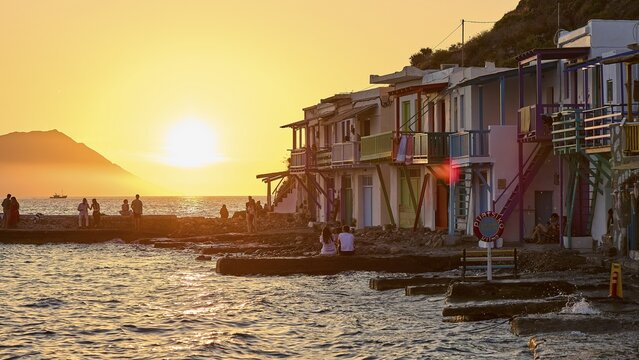 Colourful buildings along the coast at sunset with silhouettes of people and warm light, boathouses, boat garages, Syrmata, fishing village, coastal town, climate, Milos, Cyclades, Greek islands, Greece
