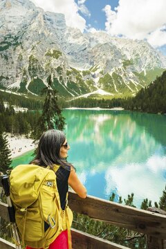 Woman Hiker traveler or visitor with Yellow Backpack Looking at Lago di Braies Dolomites Italy. Famous hiking destination Europe