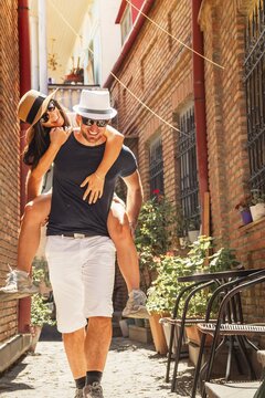 Beautiful young tourist couple Happy caucasian couple having fun piggyback visiting walk narrow alley street. Tourists enjoying holiday in Europe. Vacation and happy lifestyle concept