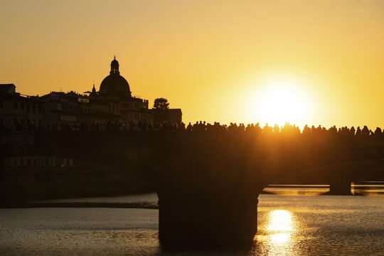 Crowd of people on a bridge over the Arno at sunset, back light, silhouette of a dome in the background, Florence, Tuscany, Italy